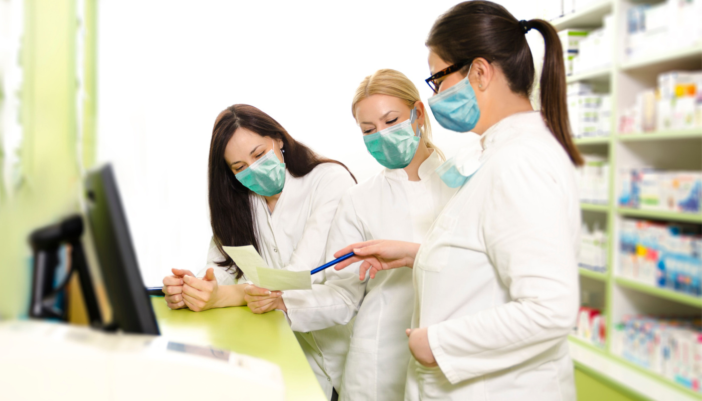 Pharmacists wearing surgical masks discussing medications and organizing their work day
