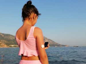 Woman checks glucose level with CGM device before entering the sea; decentralized trials concept