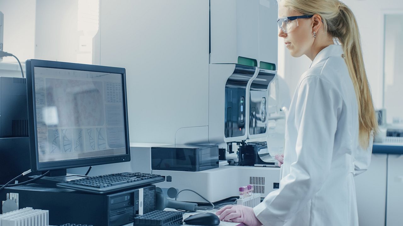 Woman in white lab coat working on a desktop; synthetic data concept