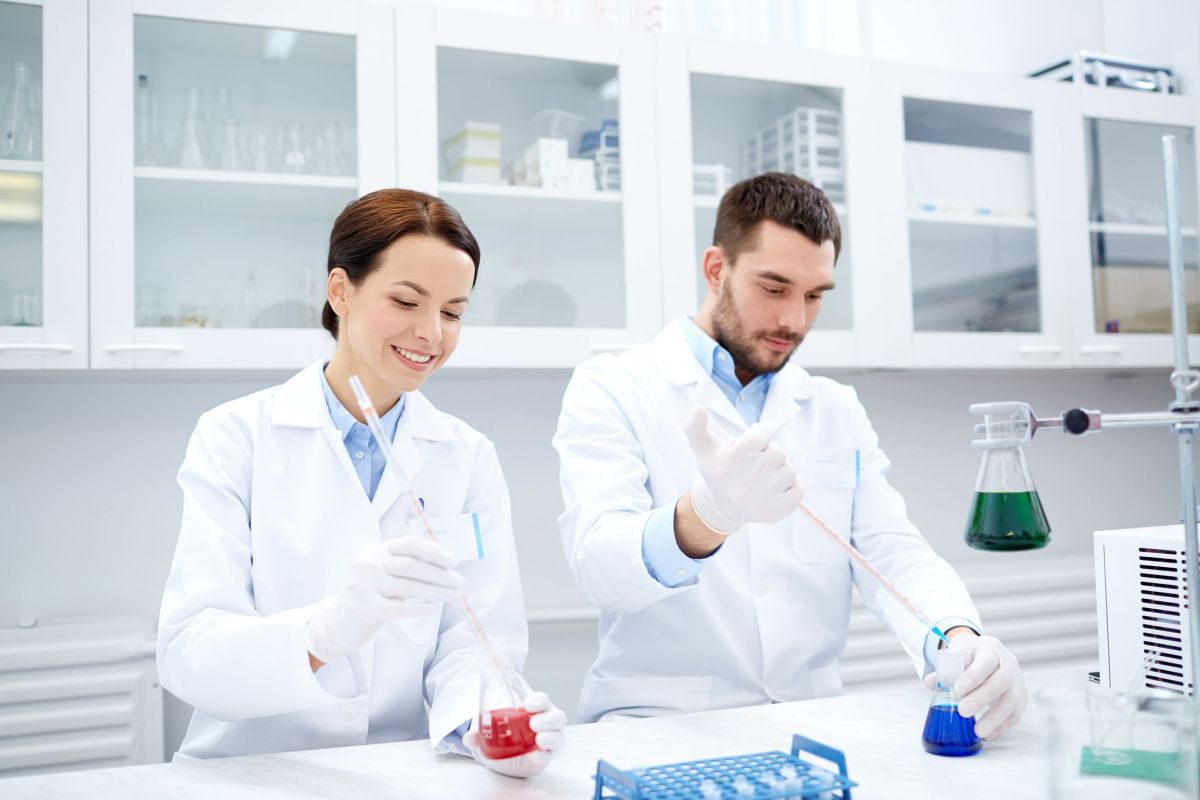 science, chemistry, technology, biology and people concept - young scientists with pipette and flask making test or research in clinical laboratory