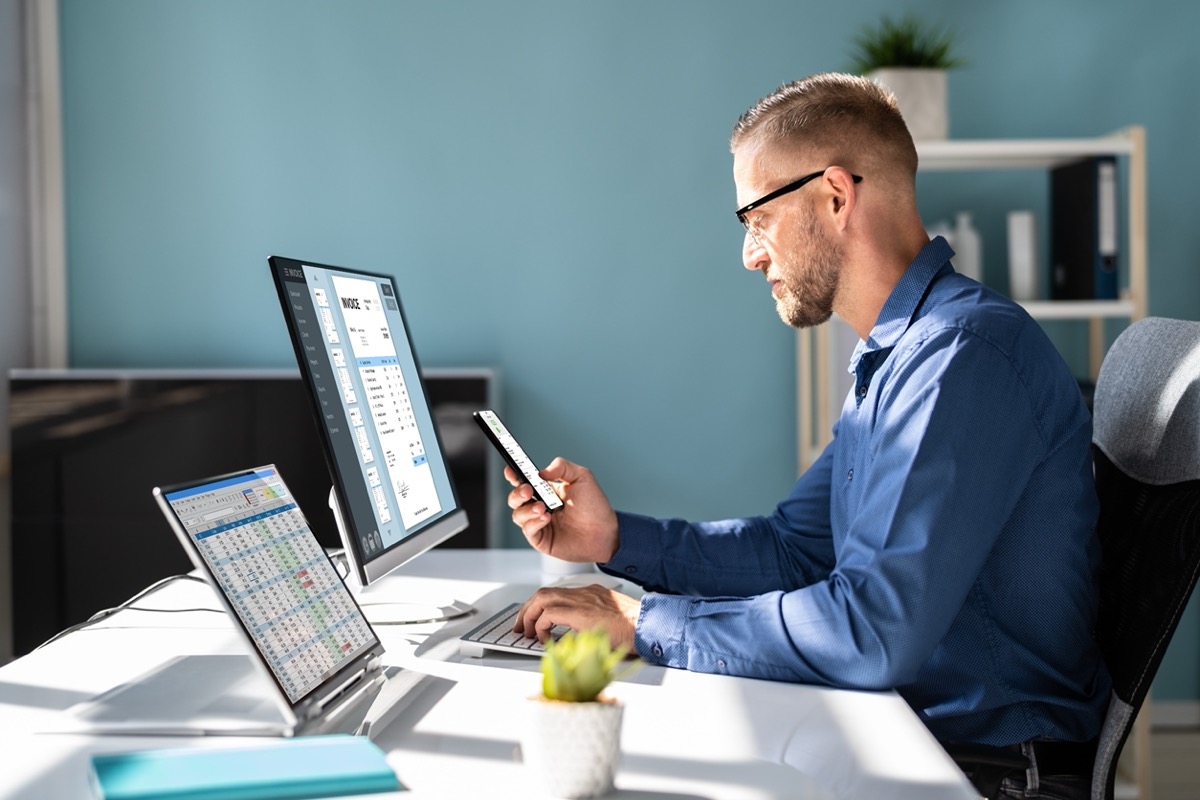 Man at desk working on two monitors and phone; quicker data collection concept