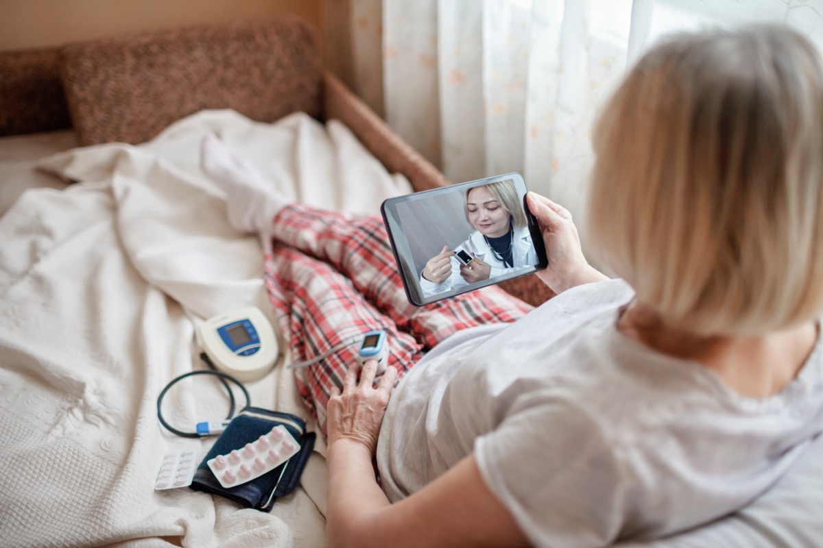 Old woman in bed looking at screen of laptop and consulting with a doctor online at home; fda decentralized trials concept