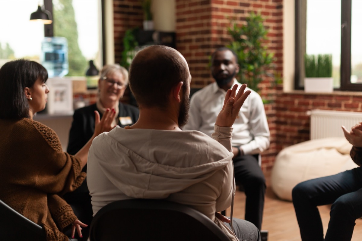 Person speaking to group of people, sitting in a circle, at a meeting; rare disease clinical trials challenges concept