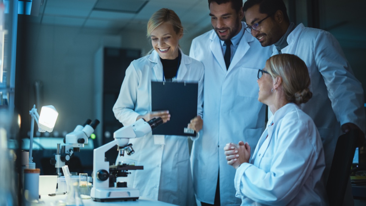 Team of smiling research scientists standing around colleague sitting in the lab; disease landscaping concept