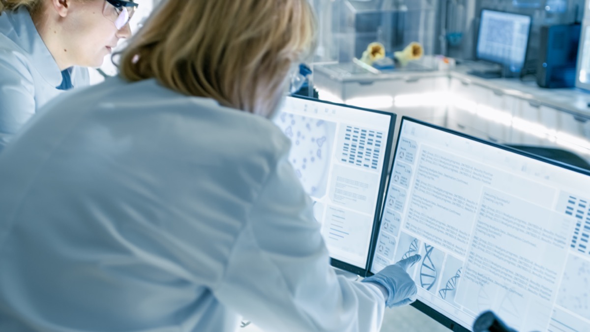 Scientist discusses data with laboratory assistant, looking at two displays in lab; regulations clinical researchers should track concept