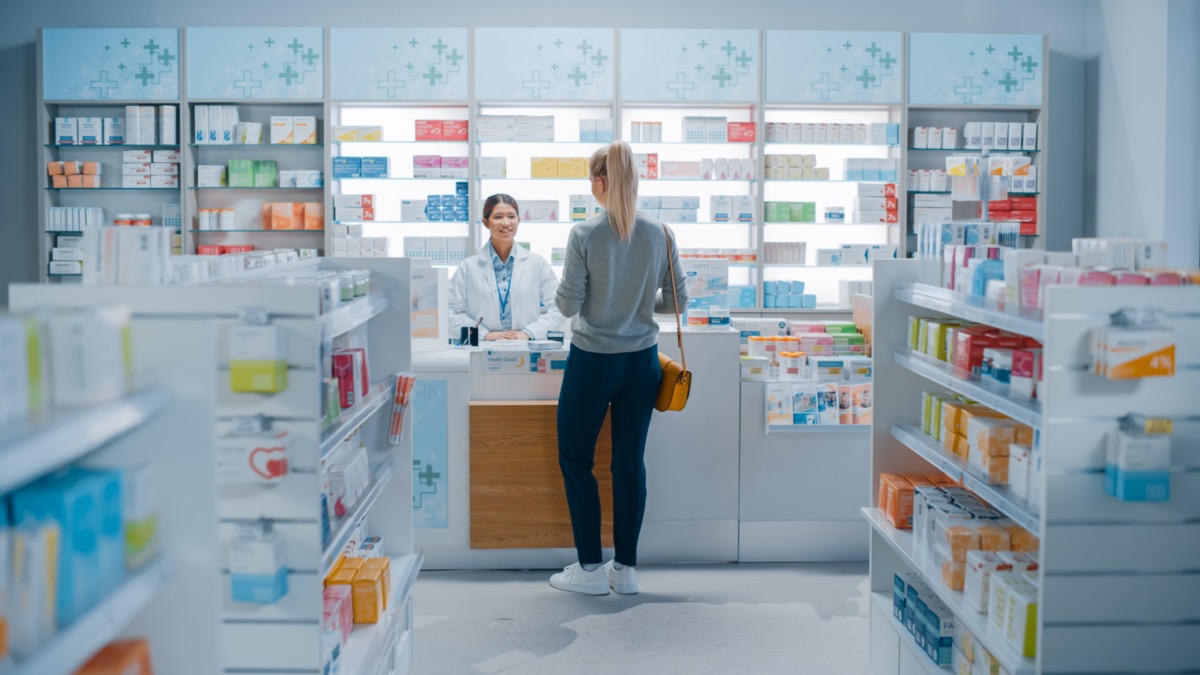 Pharmacy customer speaking to pharmacist at counter; clinical trial enrollment concept