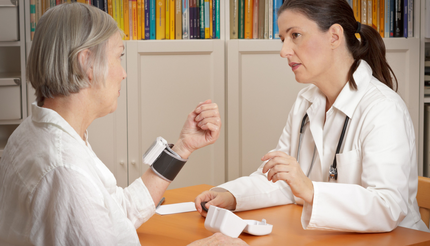 Doctor explaining the correct use of a wrist blood pressure monitor to patient; data management challenges concept