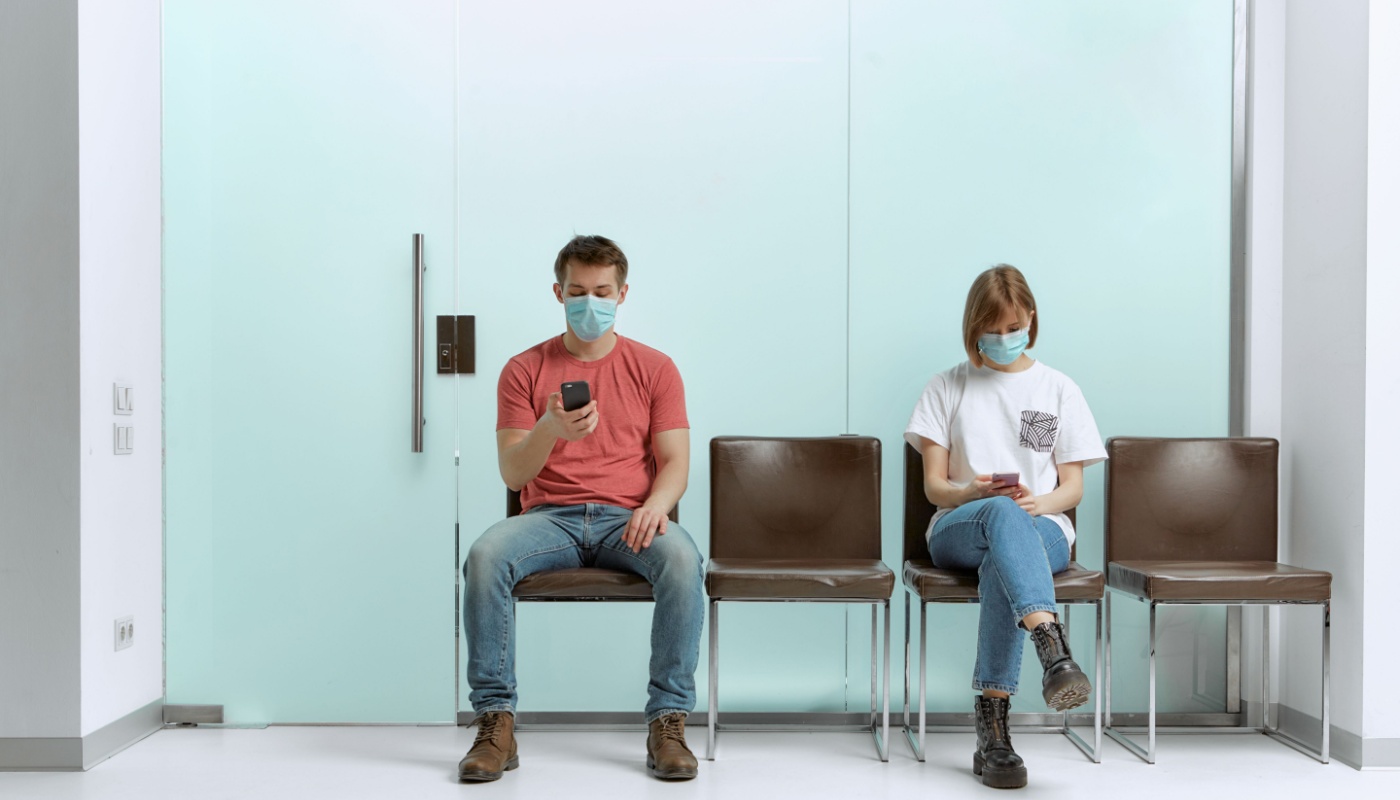 Young man and woman in medical masks, sitting in a hospital clinic's waiting room; streamlining clinical trials concept