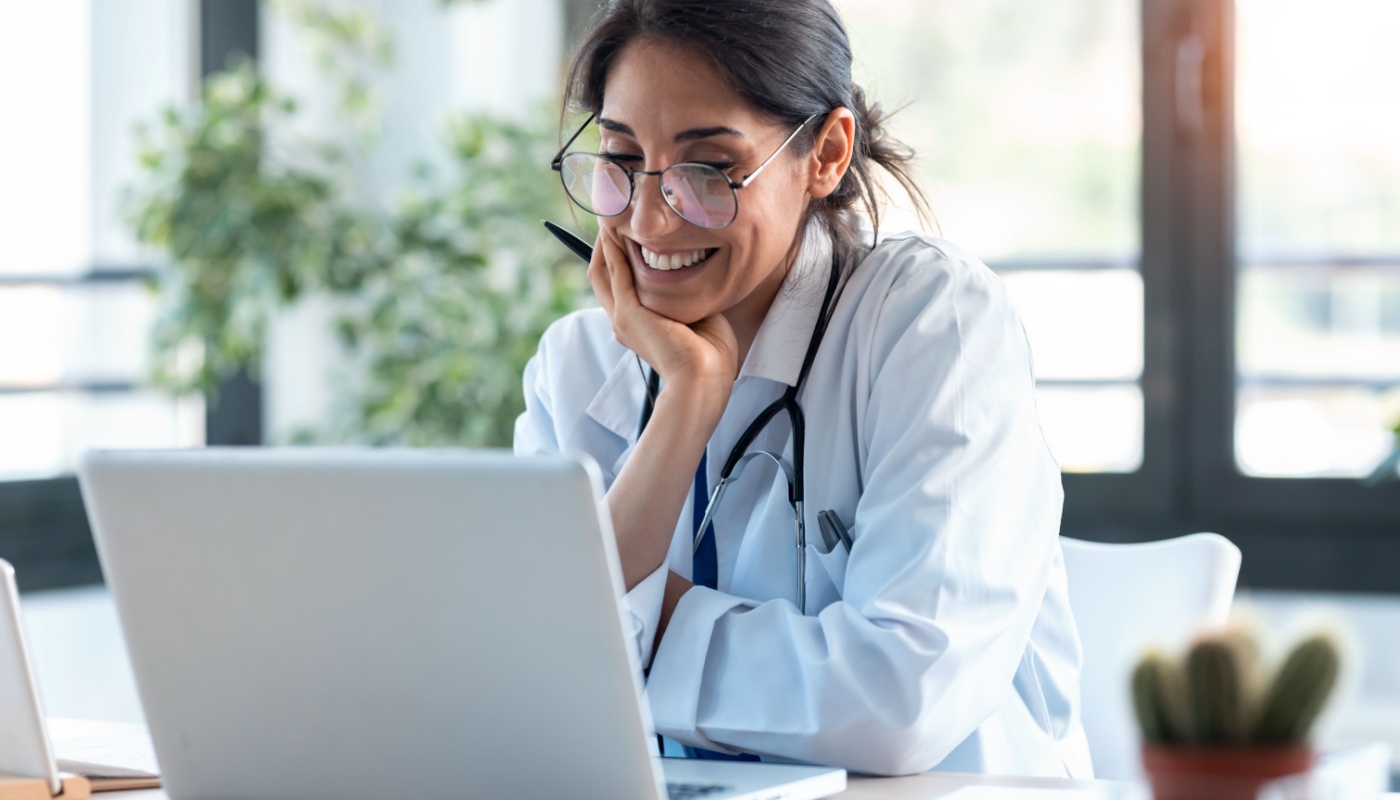 Smiling doctor using laptop for a meeting or consultation; global collaboration concept